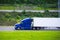 Modern dark blue semi truck reefer trailer profile on green road