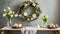 A modern Easter table decoration with a floral Easter wreath hanging on the wall