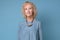 Modern elderly blonde woman standing smiling against blue background
