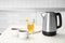 Modern electric kettle, cups of tea and honey on table in kitchen