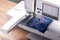 Modern embroidery machine stitching light pink magnolia graphic on classic blue boiled wool on wooden work bench