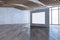Modern empty spacious concrete interior with blank white mock up banner on wall, wooden flooring, windows, city view and daylight