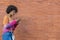Modern ethnic girl with afro hair smiles as she looks at her smartphone next to a brick wall