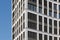 Modern facade with typical rectangular windows, reflection glass and randomly louvers against blue sky.