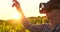 Modern farmer in VR helmet controls corn crop standing in field at sunset in sunlight