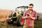 Modern farmer working and harvesting using smartphone in modern agriculture with tractor background