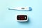 Modern fingertip pulse oximeter and digital thermometer on blue background, flat lay