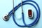 Modern fingertip pulse oximeter and stethoscope on blue background, flat lay