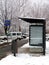 Modern glass and aluminum bus shelter in urban setting with snowy road and parked cars