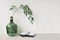 Modern green glass bottle with willow tree branch, books and glasses on beige tabletop. Empty neutral beige concrete wall