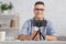 Modern hobby and remote work online. Focus on smartphone on tripod and smiling guy with glasses makes video for blog in