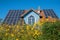 modern house with lots of photovoltaic panels at the roof, yellow topinambur flowers, blue sky