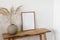 Modern interior. Beige ball vase with dray bunny tail, festuca grass. Blank vertical wooden frame picture mock up on old