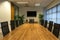 Modern interior of boardroom, meeting or seminar room with chairs and long wooden table at workplace or office, green plants and T