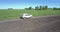 Modern jeep drives along narrow road past wide green field