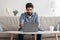 Modern job. Concentrated arab man working on laptop at home office, sitting on sofa and using computer