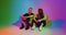 Modern joyful young teen couple having fun talking sitting on floor in colourful neon studio light. Romantic dating