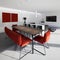 Modern living room with red bench and armchair with table lit by hanging lamps. there is a low bookcase and a large wall-mounted