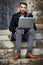 The modern man is a connected man. a handsome young man sitting on urban steps and using a laptop.