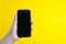 Modern media concept: hand holding a modern smartphone over yellow colorful background with copy space. Smartphone isolated. Comun