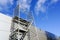 Modern metal scaffolding next to a new building gray sandwich panel wall, blue sky background