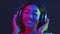 Modern music. Young asian lady wearing wireless headset enjoying dynamic music, dancing in neon lights over dark studio