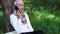 A modern Muslim woman speaks on a smartphone, she sits near a tree in the park