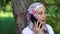 A modern Muslim woman speaks on a smartphone, she sits near a tree in the park