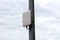 Modern new wireless communication device in white plastic case tied with plastic ties to old metal utility pole