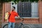 Modern online shopping with home delivery. Serious young man with beard in uniform, with yellow backpack and bicycle