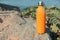 Modern orange thermos on stone near river. Space for text