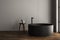 Modern oval black bathtub is standing in front gray wall and stool in empty bathroom. Minimalist concept.