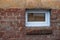 Modern plastic basement window with glare with brick shelf under it in lower part, lined with brown broken off in places bricks