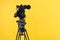 Modern professional video camera on yellow. Space for text