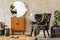 Modern retro composition of living room interior with design armchair, lamp, rattan pouf, plants, mirror, decoration, carpet.