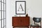 Modern retro concept of living room interior with design teak commode, black mock up poster frame, clock, chair, decoration.