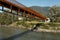 Modern rusted pedestrian and bicycle bridge with flowing Ticino river below. Beautiful panorama of the Alps of Italian Switzerland