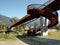 Modern rusted pedestrian and bicycle bridge with flowing Ticino river below. Detail of the spiral staircase and mountain panorama