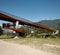 Modern rusted pedestrian and bicycle bridge with flowing Ticino river below. Mountain panorama of the Swiss Alps on a sunny summer