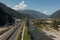 Modern rusted pedestrian and bicycle bridge with flowing Ticino river below. On the other side of the river is a highway under