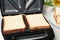 Modern sandwich maker with bread slices on light grey table, closeup