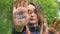 Modern serious girl with long dreadlocks is showing hands with written slogan `Our future in your hands` on green tree