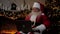 Modern smiling old Santa Claus uses laptop fills in holiday cards for children