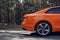 A modern sports orange car is parked on a forest road. Travel concept. View of the rear wheel and the rear of the car