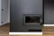 A modern standing fireplace in the living room enclosed with panels, painted black with a corner pane covered with soot.