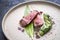 Modern style barbecue dry aged sliced fillet steak with wild garlic and zucchini on a design plate with hot sp