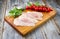 Modern style raw traditional chicken escalope with tomatoes and herbs on a design wooden board