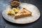 Modern style traditional French Tarte au citron piece with orange and physalis fruit on a rustic design plate