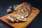 Modern style traditional Italian Porchetta arrotolata pork meat sliced and as piece with herbs and figs on a wooden design board