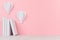 Modern style workplace - white pile books as bookcase and decorative paper balloons on soft pink background and light desk.